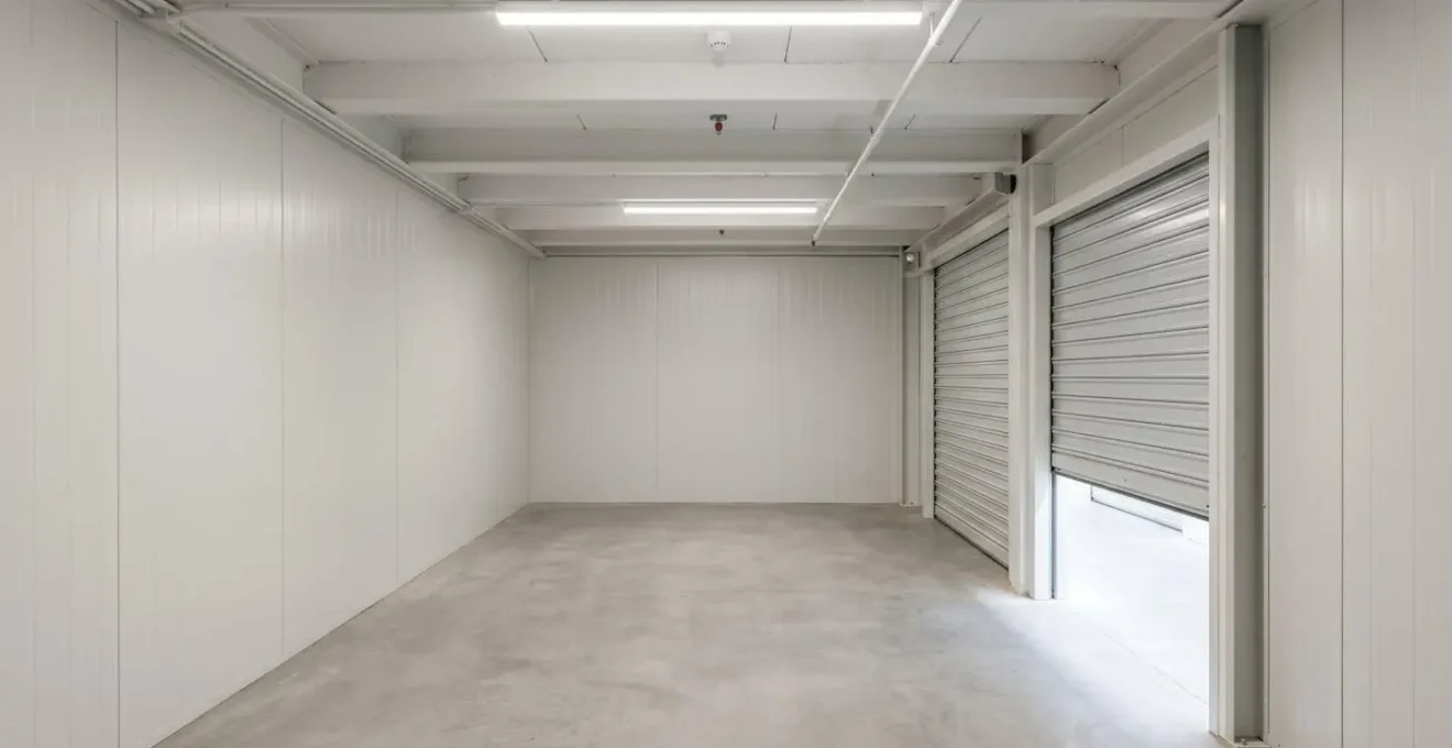 Intérieur vide d'un box de stockage professionnel avec murs clairs, sol béton propre, détecteur de fumée au plafond et éclairage LED uniforme